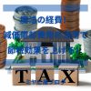 「魔法の経費！減価償却費用の活用で節税効果を上げる！」のイメージ画像。TAXと書かれた積み木の後ろに、家の模型と積み上げられたコインがある。